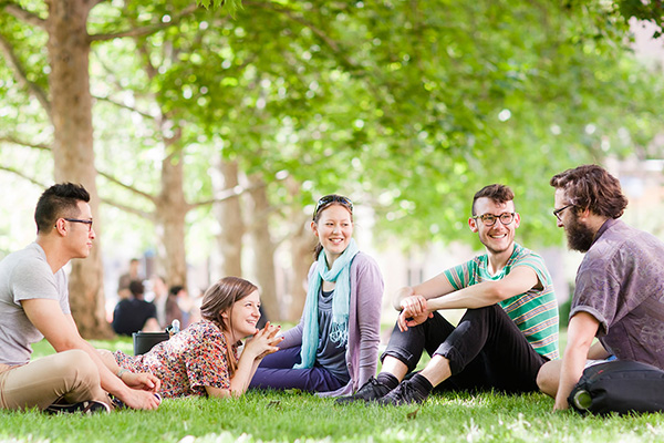 Students sitting on grass under trees talking